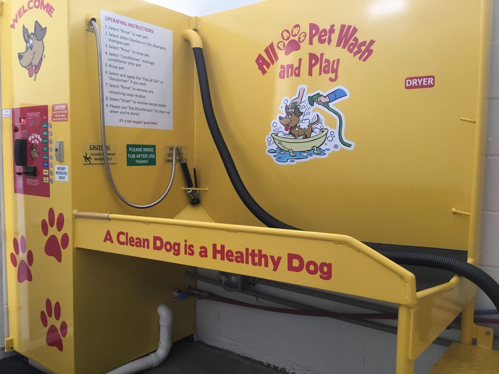 A yellow self-serve dog wash station with hoses and a dryer